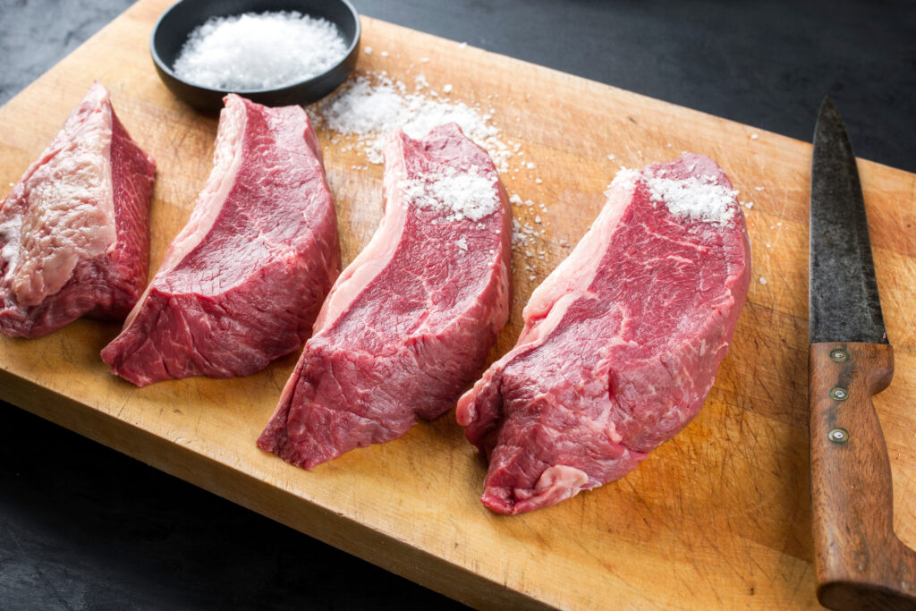 Raw dry aged wagyu cap of rump beef sliced for picanha barbecue skewer with salt offered as close-up on a wooden rustic cutting board