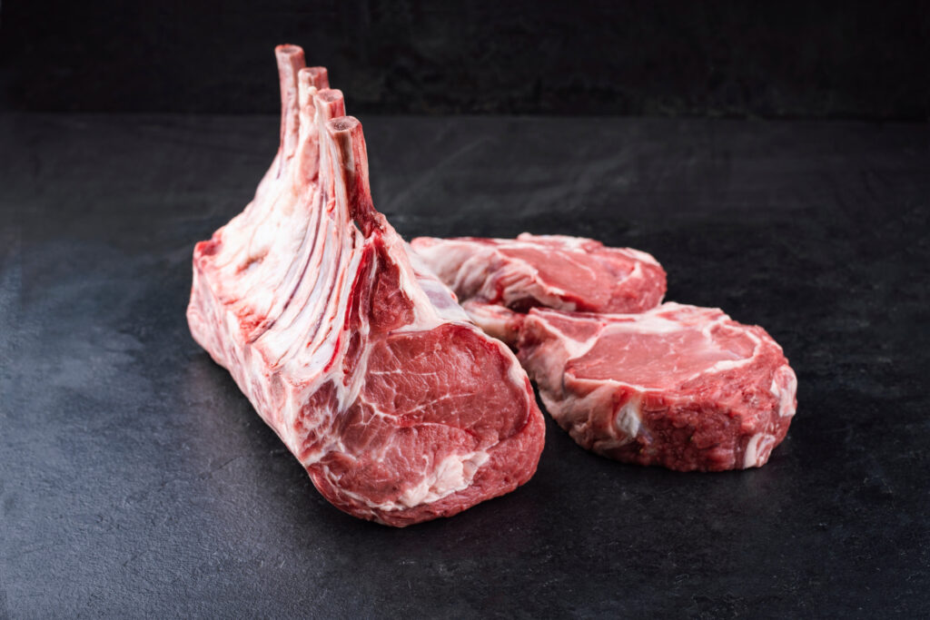 Raw dry aged bone-in back rack of veal loin offered as close-up on a black board