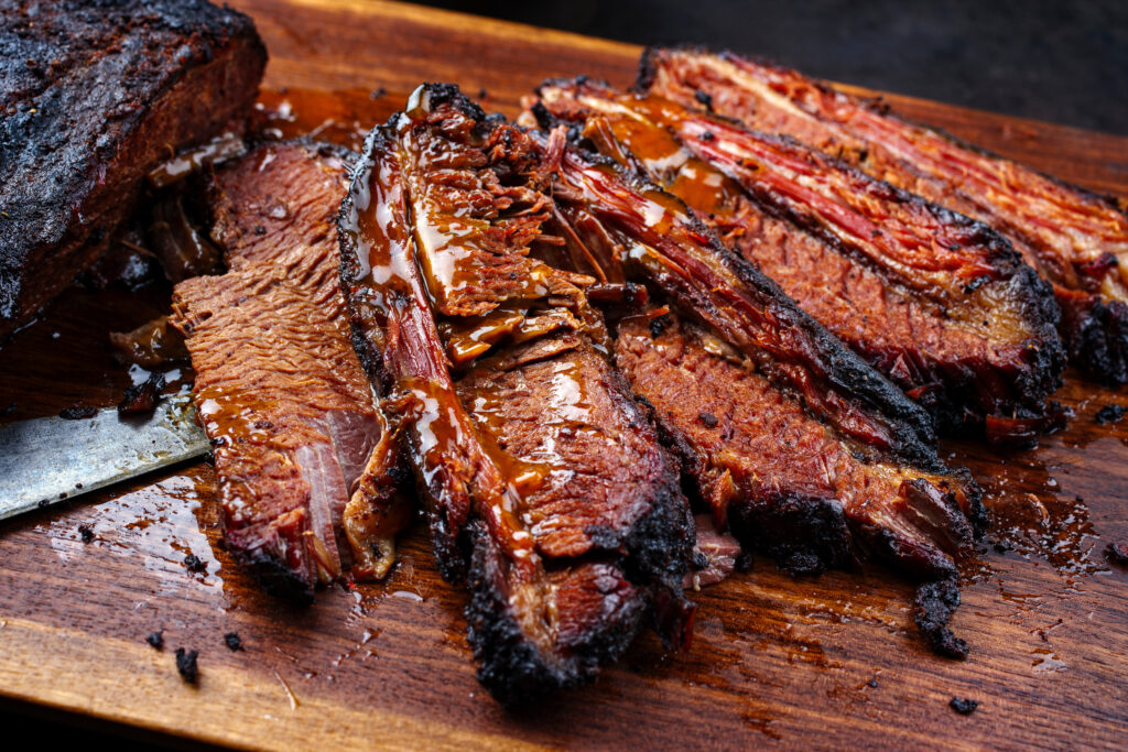 Modern style traditional smoked barbecue wagyu beef brisket served as top view on a wooden design cutting board with Louisiana sauce