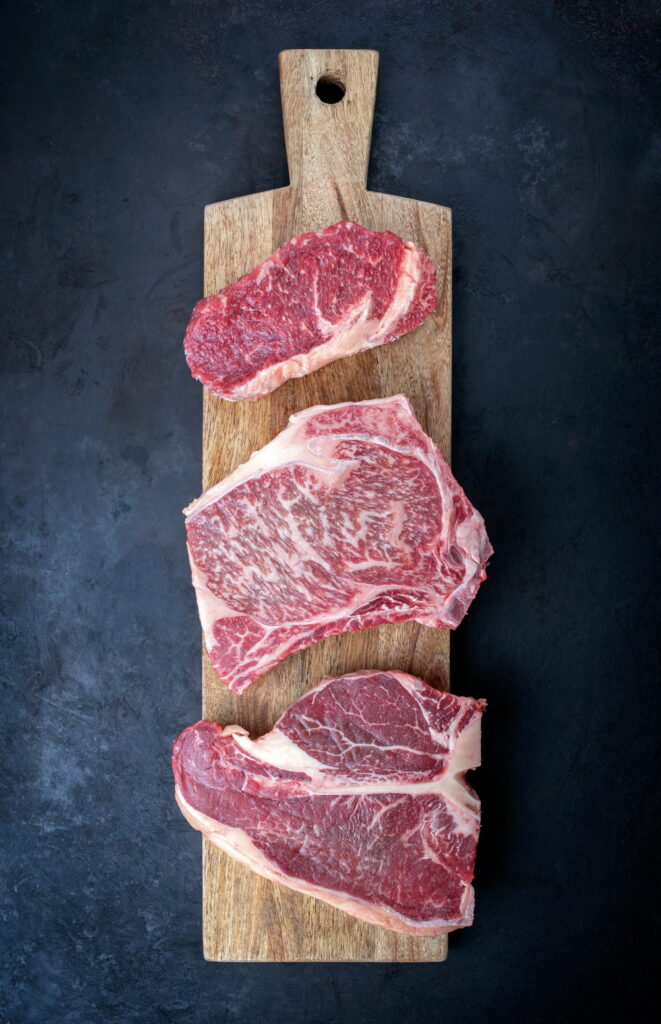 Raw dry aged wagyu porterhouse beef steak, entrecote and cutlet offered as top view on wooden board with copy space